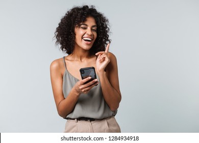 Happy Young African Woman Casually Dressed Standing Isolated Over Gray Background, Using Mobile Phone