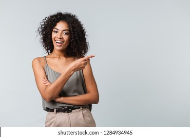 Happy young african woman casually dressed standing isolated over gray background, pointing away