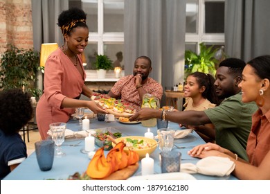 Happy young African woman putting appetizing vegetarian sandwiches for big family on festive table while her son or nephew helping her