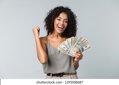 Happy Young African Woman Standing Isolated Over Gray Background, Holding Bunch Of Money Banknotes, Celebrating