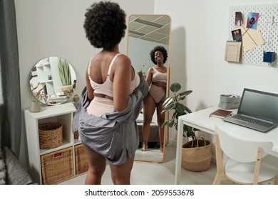 Happy Young African Woman In Underwear Looking At Herself While Standing In Front Of Large Mirror