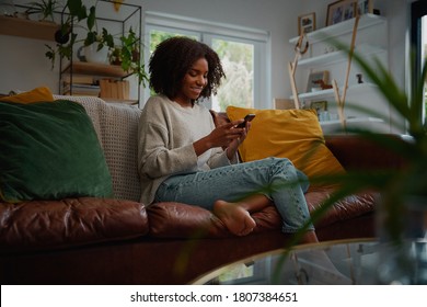 Happy Young African Woman Using Mobile Phone While Sitting A Couch At Home