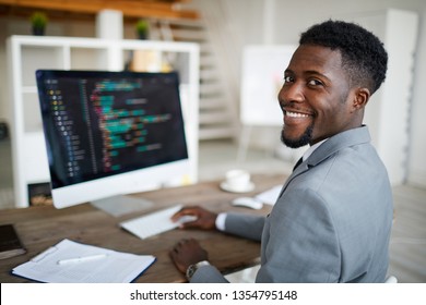 Happy Young African-american Software Developer In Formalwear Sitting By Workplace In Front Of Computer Screen With Decoded Data