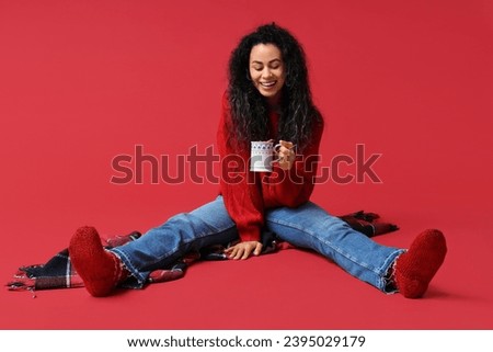 Happy young African-American woman with cup of hot mulled wine on red background