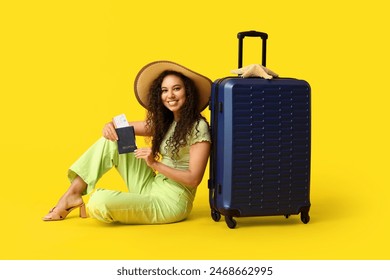 Happy young African-American woman in hat with suitcase, passport and ticket sitting on yellow background. Travel concept - Powered by Shutterstock