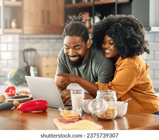 Happy young afro american couple having fun preparing food and looking for recipes online using a laptop in kitchen - Powered by Shutterstock