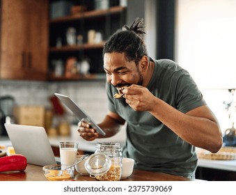 Happy young afro american man having fun preparing food and looking for recipes online using atablet and a  laptop in kitchen, or a young businessman working from home office