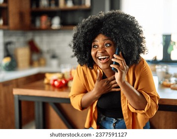 Happy young afro american woman having fun preparing food and a mobile phone in kitchen, or a young businesswoman working from home office making connections online, talking making a phone call - Powered by Shutterstock