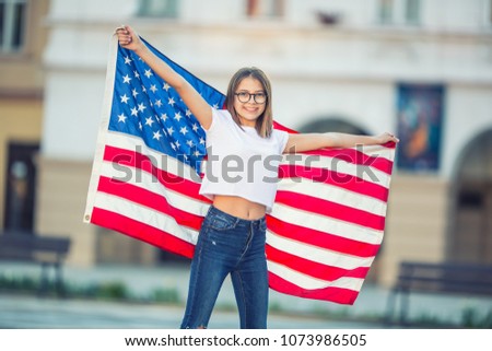 Happy young american school girl holding and waving in the city with USA flag. 