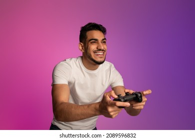 Happy young Arab guy with joystick playing video game in neon light. Millennial middle Eastern gamer with controller participating in online gaming championship. Modern hobbies concept - Powered by Shutterstock