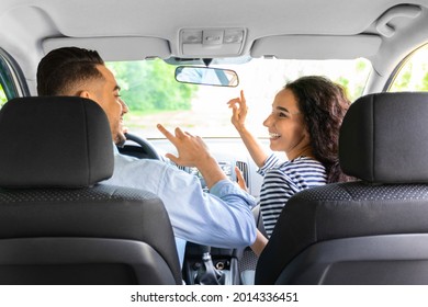 Happy Young Arab Man And Woman In Casual Outfit Having Fun While Going Vacation By Car, Dancing And Singing Songs, Shot From Auto Back Seat. Entertainment While Car Trip, Fun, Joy Concept