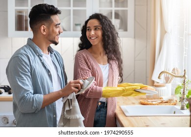 Happy Young Arab Spouses Washing Dishes In Kitchen Together, Loving Middle Eastern Couple Sharing Domestic Chores, Millennial Man And Woman Cleaning Home And Smiling To Each Other, Copy Space