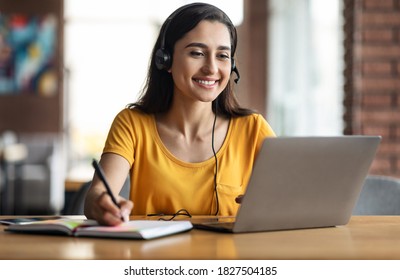 Happy young arab woman having educational course online, using laptop and headset, cafe interior, free space. Smiling female student studying online, sitting in front of laptop at cafeteria - Shutterstock ID 1827504185