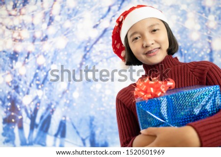 Happy young asia girl hold present box with snow background.