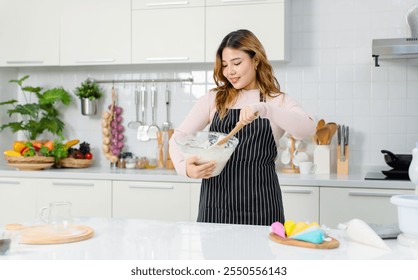 Happy young Asian beautiful female wearing apron looking at camera smiling holding bowl while kneading dough for baking cakes woman making homemade bread, dessert. Cooking concept weekends in kitchen - Powered by Shutterstock