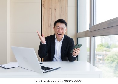 Happy Young Asian Business Man In Office, Looking At Camera, With Emotions Of Winner Or Victory, Financial Promotion Sports Betting. The Man Exclaims Happily While Playing The Game. Excited With Joy, 