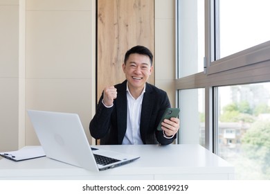 Happy Young Asian Business Man In Office, Looking At Camera, With Emotions Of Winner Or Victory, Financial Promotion Sports Betting. The Man Exclaims Happily While Playing The Game. Excited With Joy, 