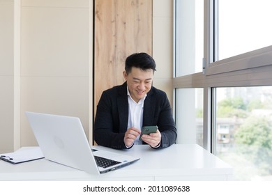 Happy young Asian business man in office looking at mobile phone, with emotion winner or win, financial stock sports betting. Male joyfully exclaims playing game. Excited overjoyed celebrating success - Powered by Shutterstock