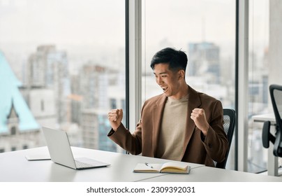 Happy young Asian business man celebrating success at work in office looking at laptop excited about financial trading growth, goals achievement good online results, screaming yes watching game. - Powered by Shutterstock