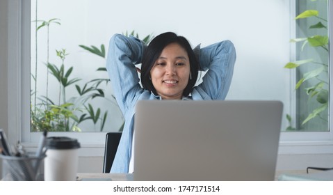 Happy young asian business woman looking at laptop computer, smiling and stretching her arms during online working in modern office. Confident businesswoman being  proud of her successful work