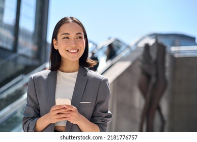 Happy young Asian business woman standing on urban street using cell phone. Smiling lady wearing suit holding smartphone outside advertising modern smart city apps, mobile applications. - Shutterstock ID 2181776757