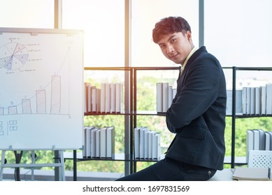 happy young asian businessman in formal dress sitting on table corner crossed hand in smart relax in modern office with computer laptop on table in workplace. - Shutterstock ID 1697831569