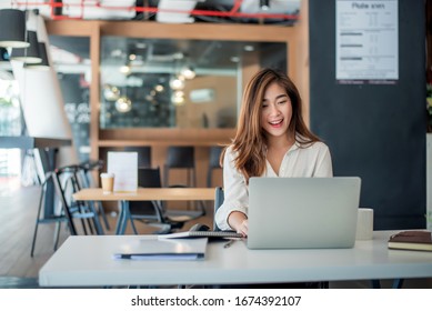 Happy young asian businesswoman sitting on her workplace in the office. Young woman working at laptop in the office.