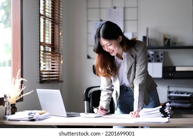 Happy Young Asian Businesswoman Standing Using Calculator And Laptop Computer At Office.
