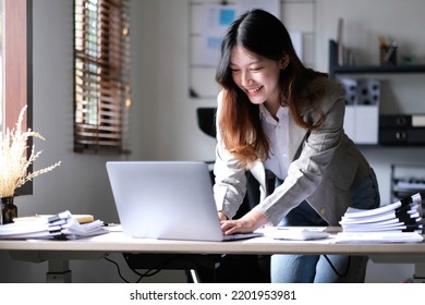 Happy Young Asian Businesswoman Standing Using Calculator And Laptop Computer At Office.
