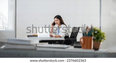 Happy young asian businesswoman talk on the mobile phone and smile while sitting at working place in office