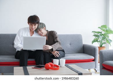 Happy Young Asian Couple Gay Lovers Sitting Snuggle And Using Laptop Computer Together On Sofa At Living Room At Home. LGBT Lifestyle And Relationship Concept