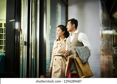 Happy Young Asian Couple Looking Into Window Of A Shop In Shopping Mall