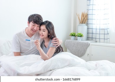 Happy Young Asian Couple Smiling After Find Out Positive Pregnancy Test On Bed In Bedroom
