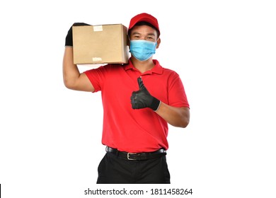 Happy Young Asian Delivery Man In Red Uniform, Medical Face Mask, Protective Gloves Carry Cardboard Box In Hands Isolated On White Background. Delivery Guy Give Parcel Shipment. Safe Delivery