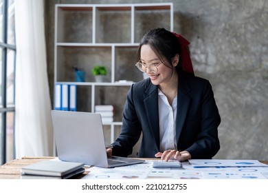 Happy Young Asian Entrepreneur Woman In Glasses Counting Profit, On Calculator At Laptop Computer, Analyzing Benefits, Enjoying Financial Success.