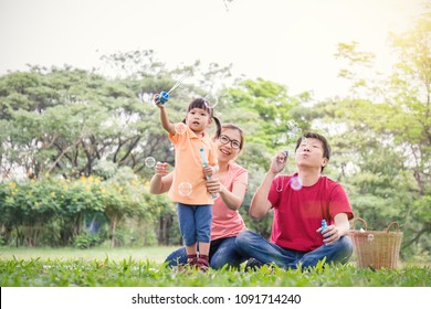 Happy young asian family playing with bubble wands with daughter in park outdoors in summer or spring. Together community love fresh green eco lifestyle family day concept