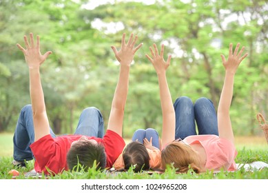 Happy young Asian family with their daughter are lying and raised hands up on green grass in nature at park outdoor. Holiday and Having fun.