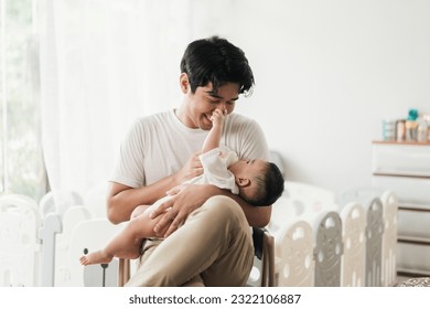 Happy young Asian father feeding cute baby boy with milk from baby bottle. Little baby drinking milk and touching on face father. Fathers day concept.