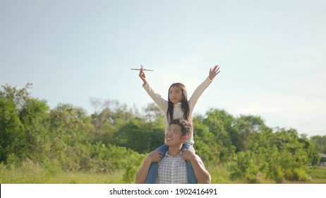 Happy Young Asian Father Piggyback With His Little Girl, She Play The Toy Airplane And Have Enjoyed Ourselves Together In The Green Garden. Family Enjoying Sunny Fall Day In Nature.