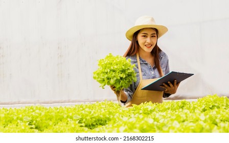 Happy Young Asian Female Farmer Holding Clipboard Working In Industrial Agriculture Organic Hydroponics Vegetable Farm Produce Organic For The Quality And Integrity Of Our Online Delivery Business.