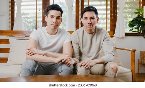 Happy Young Asian Gay Couple Sit Couch Use Smartphone Facetime Video Call With Friends And Family In Living Room At Home. Stay At Home Quarantine, Social Distancing, LGBTQ+ Young Married Concept.