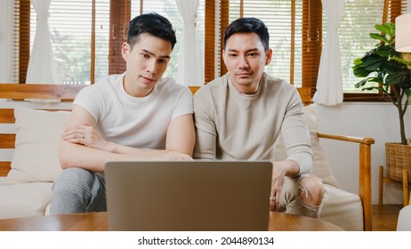 Happy Young Asian Gay Couple Sit Couch Use Laptop Facetime Video Call With Friends And Family In Living Room At Home. Stay At Home Quarantine, Social Distancing, LGBTQ+ Young Married Concept.