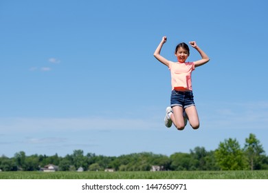 Happy Young Asian Girl Jumping High In Air, Against Background Of Summer Blue Sky.