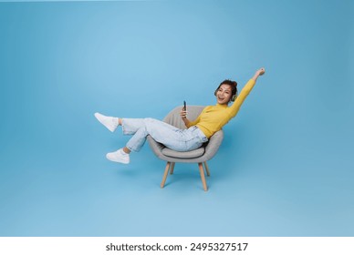 Happy young asian girl listening music with headphone dancing on chair isolated on blue background. People lifestyle concept - Powered by Shutterstock