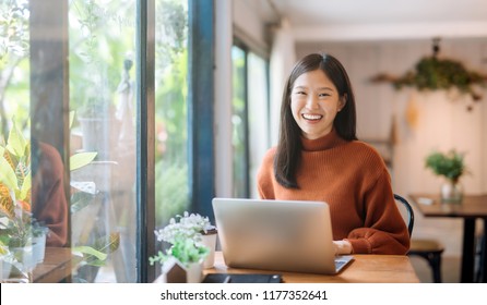 Happy young Asian girl working at a coffee shop with a laptop 