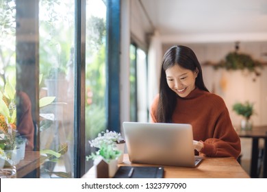 Happy young Asian girl working at a coffee shop with a laptop.