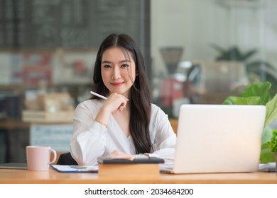 Happy Young Asian Girl Working At A Coffee Shop With A Laptop.Woman Happy Smiling To Camera In Cafe Day
