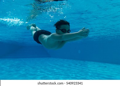 Happy young asian kid with swim goggles underwater - breast stroke in middle of swimming pool, smile relax face swimmer have fun activity