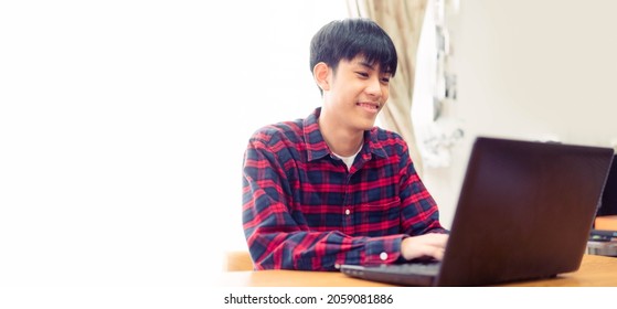 Happy Young Asian Male Smiling Using Laptop At Home.Work From Home.Isolated Banner Background.Teenager Young Boy Online Learning Typing Social Chat.Social Media.University Male, Blogger Freelance Man.