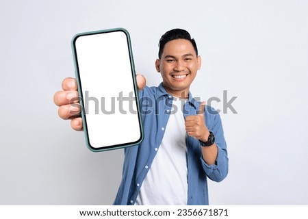 Happy young Asian man in casual shirt showing smartphone with blank screen and thumb up isolated on white background